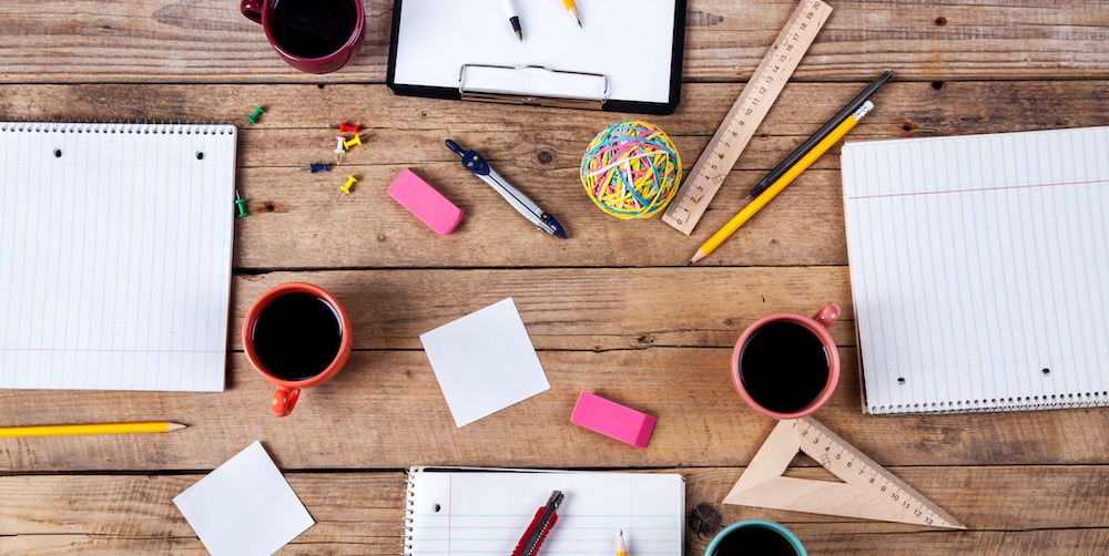 Table with notepads, coffee and pencils.